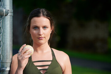 Gorgeous young female fitness model poses outdoors holding baseball