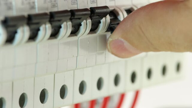 The hand turns on the circuit breaker of the current in the electrical switchboard. Soft focus. 