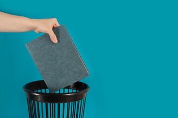 Hand throwing law book into the trash bin or waste bucket. Outdated literature, waste paper concept