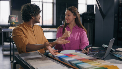 Multiracial couple creative designers work in modern office studio Arabian Indian man Caucasian woman using phone choosing perfect sample of material color tone for new house interior design project