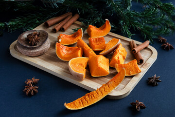 Roasted Pumpkin on a Wooden Board with Fir Branch, Cinnamon, Anise, and Coffee Beans on a Black Background