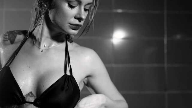Sexy woman fashion model takes a shower in a swimsuit, posing for the camera. Monochrome photography.