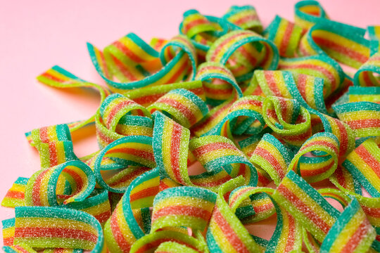 Tasty rainbow sour belts on pink background, closeup