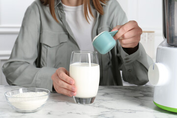 Making protein cocktail. Woman adding powder into glass with milk at white marble table, closeup