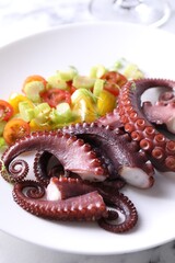 Plate with tasty boiled octopus tentacles and salad on light table, closeup