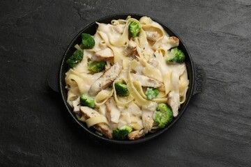 Delicious pasta Alfredo with chicken, cheese, creamy sauce and broccoli on black table, top view