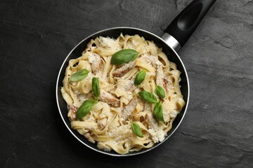 Delicious pasta Alfredo with chicken, cheese and basil in frying pan on black table, top view