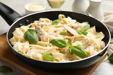Delicious pasta Alfredo with chicken, cheese and basil in frying pan on table, closeup