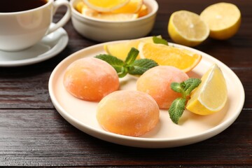 Plate with tasty mochi, cut orange, lemon and mint on wooden table, closeup