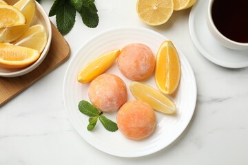Plate with tasty mochi, cut orange, lemon and mint on white marble table, flat lay