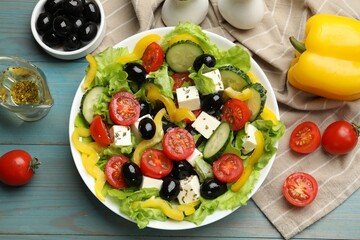 Delicious fresh Greek salad and ingredients on light blue wooden table, flat lay