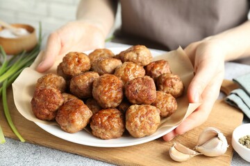 Woman holding plate with delicious meatballs at light textured table, closeup