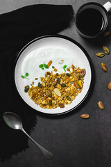 Granola in a white enamel bowl, garnished with a mint leaf, dried fruit and nuts, creates a delicious combination of textures and flavours against a dark table backdrop. The perfect breakfast or snack