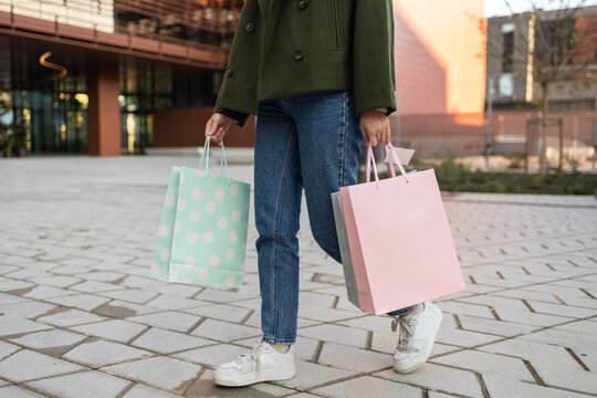 Woman in casual outfit carrying pastel shopping bags outdoors