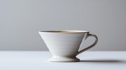 Fototapeta premium A single, off-white ceramic coffee cup with coffee sits on a white surface against a gray background.