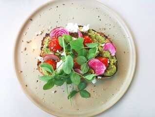 Smashed avocado on sourdough garnished with red onions and pea shoots