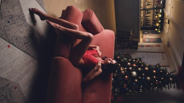 Beautiful brunette posing sexy on camera in red lace bodysuit while sitting on sofa