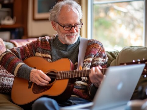 A senior man playing the guitar at home, sitting on his couch with a coffee and laptop nearby. 