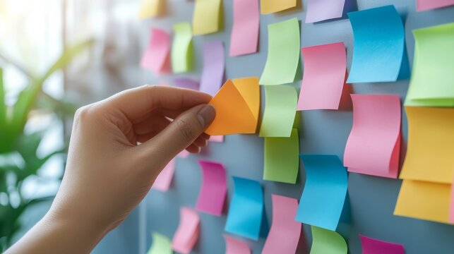 Colorful Sticky Notes on a Wall with a Hand Removing an Orange Note for Organization and Productivity in a Creative Workspace Setting