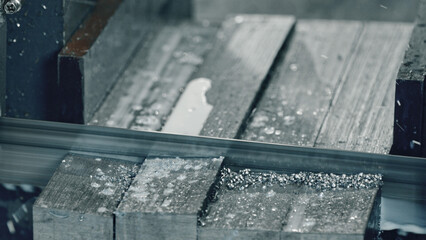 Industrial band saw cutting metal profile with coolant, producing metal shavings and creating precise cuts in a modern workshop environment