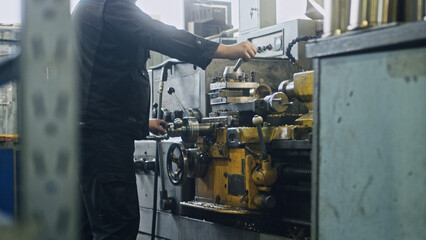 Metalworker operating industrial lathe machine, producing metal parts in a factory setting, showcasing precision and manufacturing processes