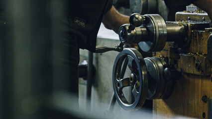 Close up of a metalworker operating an industrial lathe machine, turning a metal wheel, with metal shavings scattered around, in a workshop environment