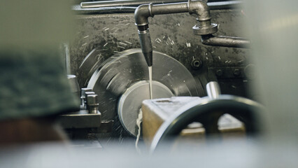 Industrial lathe machine cutting metal part with coolant in factory, producing swarf and showing...