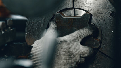 Close up of a factory worker's gloved hand positioning a metal component within a large industrial machine, showcasing precision and skill in metalworking