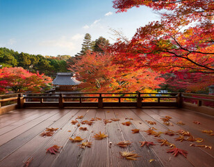 Obraz premium A traditional Japanese temple deck is covered with scattered maple leaves while surrounded by vibrant red autumn foliage against a blue sky.