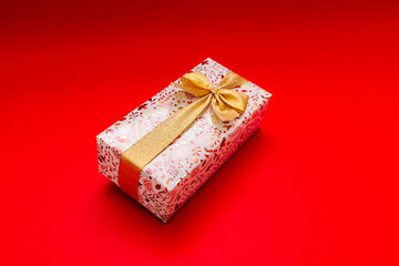 The wrapped gift on a bright red background with a gold ribbon, a gift for a birthday, Valentine's Day, New Year.