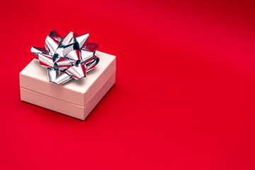 small white gift box with silver ribbon and bow on a bright red background 