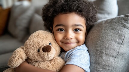 Child smiles joyfully while cuddling a soft teddy bear on a comfortable sofa in a warm living room