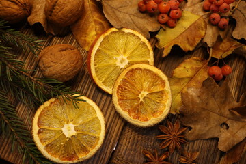 
close-up of dry leaves, spruce twig, red viburnum and star anise, nuts and oranges on a wood background