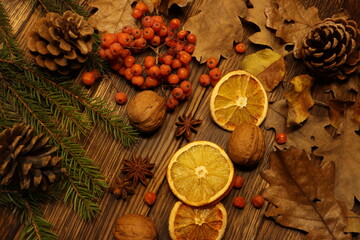 dark wooden background, fir branch in the background with pine cones, dried oranges, red viburnum and star anise candle, nuts, pomegranate, cinnamon stick  and dry leaves