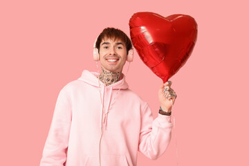 Handsome young man with headphones and heart-shaped air balloon on pink background. Valentine's Day celebration