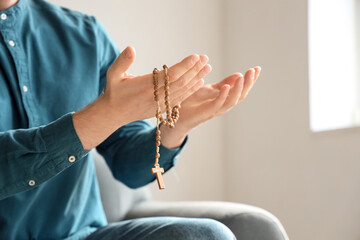 Man with rosary beads praying at home, closeup