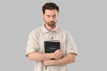 Religious man with Bible praying on grey background