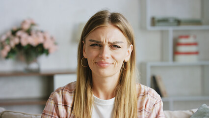 Young woman wearing casual clothes frowning on a sofa in her living room, expressing clear disgust...