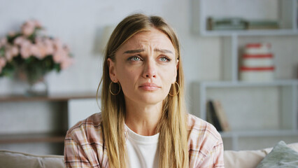 Young woman is crying on the sofa at home, she is feeling depressed and lonely, suffering from...