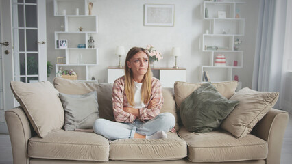 Sad woman sitting on comfortable sofa with crossed arms and crying because she is having problems, feeling desperate and lonely in her apartment