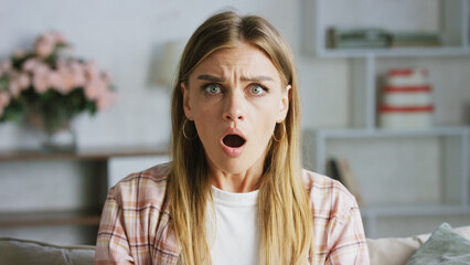 Surprised young woman opening her mouth and raising her eyebrows in disbelief while staring at...