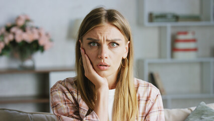 Young woman feeling toothache at home sitting on sofa touching cheek suffering from pain with worried expression having dental problem and tooth decay health issues