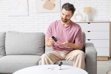 Diabetic young man using glucometer on sofa at home