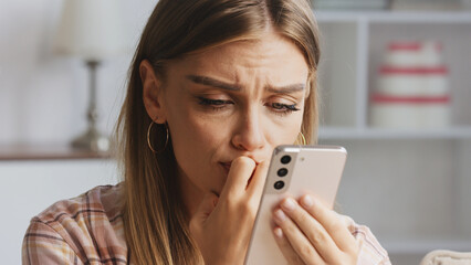 Young woman biting her nails while reading distressing news on her smartphone, feeling overwhelmed by the anxious message received, reflecting deep stress and concern in her expression