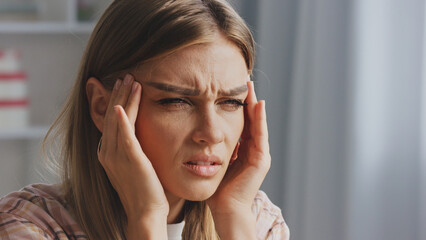 Stressed young woman touching her temples, suffering from a strong migraine or headache, feeling...