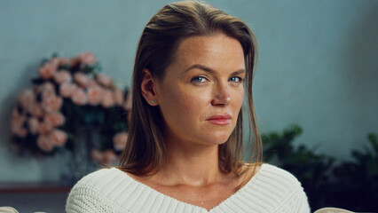 Confident and determined woman poses with a neutral expression, wearing a white sweater, with soft...