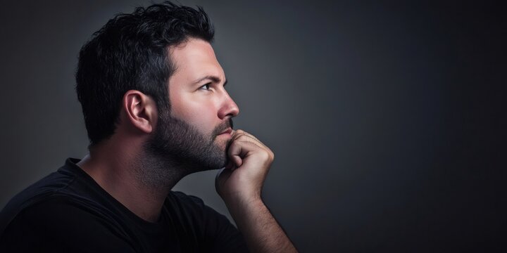 Pensive businessman resting hand on chin, gazing contemplatively against shadowy backdrop, symbolizing deep professional reflection