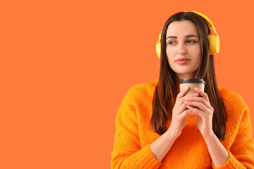 Wondering young woman in headphones with coffee cup on orange background, closeup