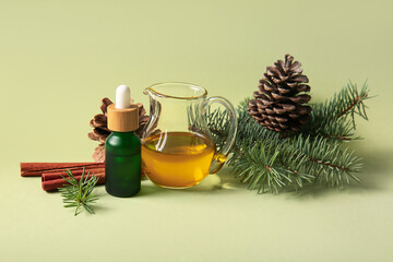 Bottle and jug of essential oil with pine cones, fir branches and cinnamon on green background