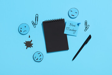 Notebook with office stationery, drawn sad faces and text BLUE MONDAY
